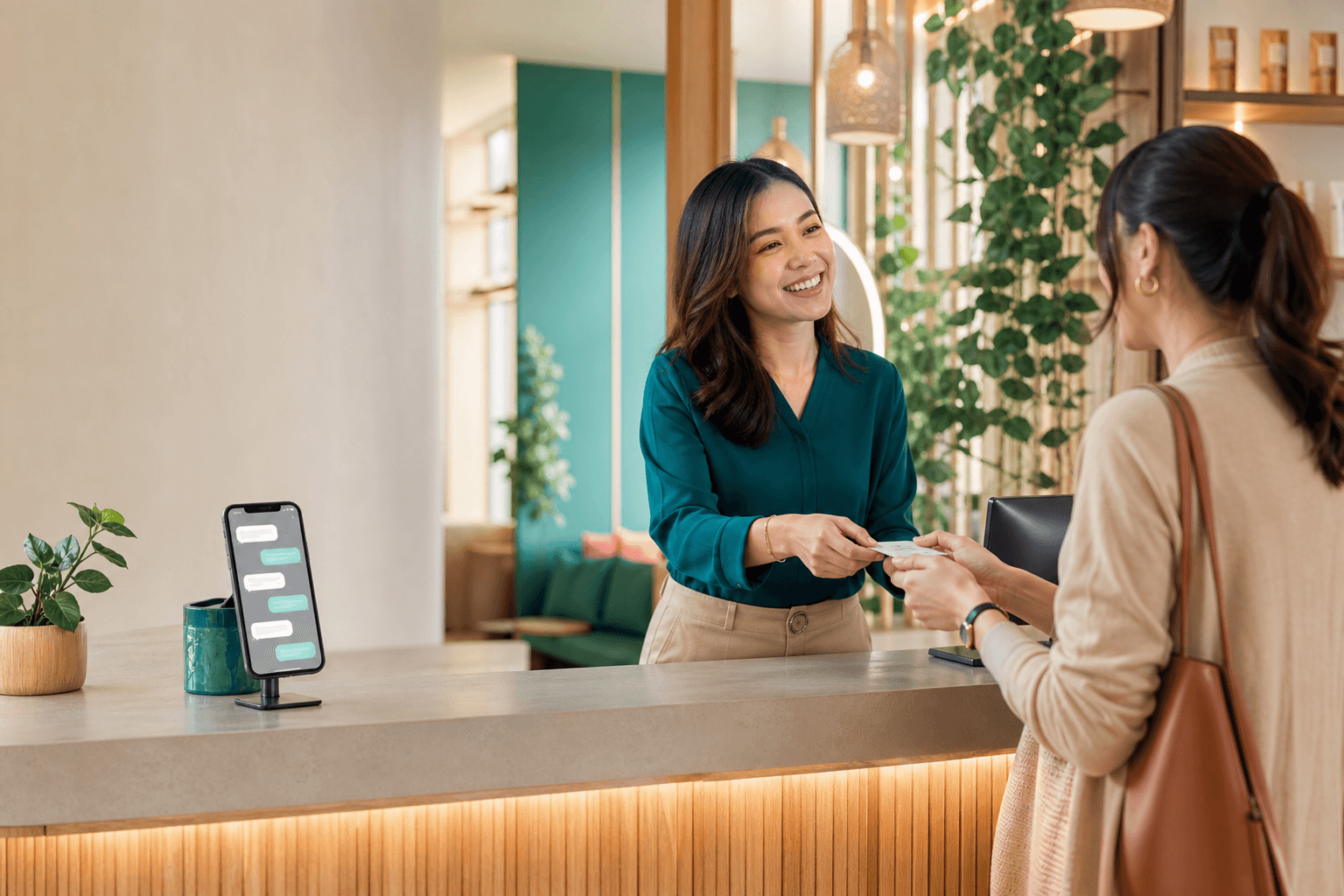 A Malaysian service-business receptionist welcoming a customer while incoming enquiries appear on a nearby phone